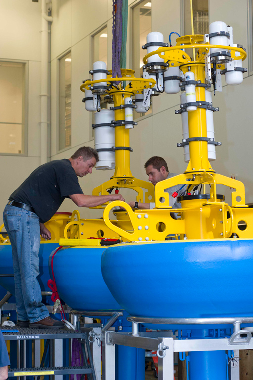 As preparations continue, WHOI Senior Engineering Assistants Jim Dunn (left) and Kris Newhall (right) prepare surface buoys for the Pioneer Array Coastal Profiler Moorings. The buoy towers house electronics and antennas (white cylinders) to enable real-time data transfer and two-way command and control from shore.